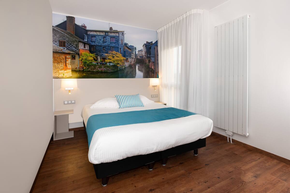 Une chambre avec un grand lit, une fresque représentant un canal, un radiateur blanc et deux lampes fixées au mur.