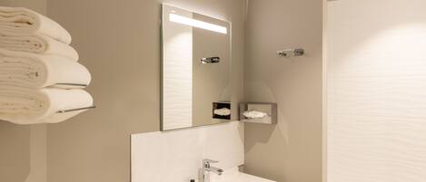 A modern bathroom with a white sink, a mirror, and a towel rack.