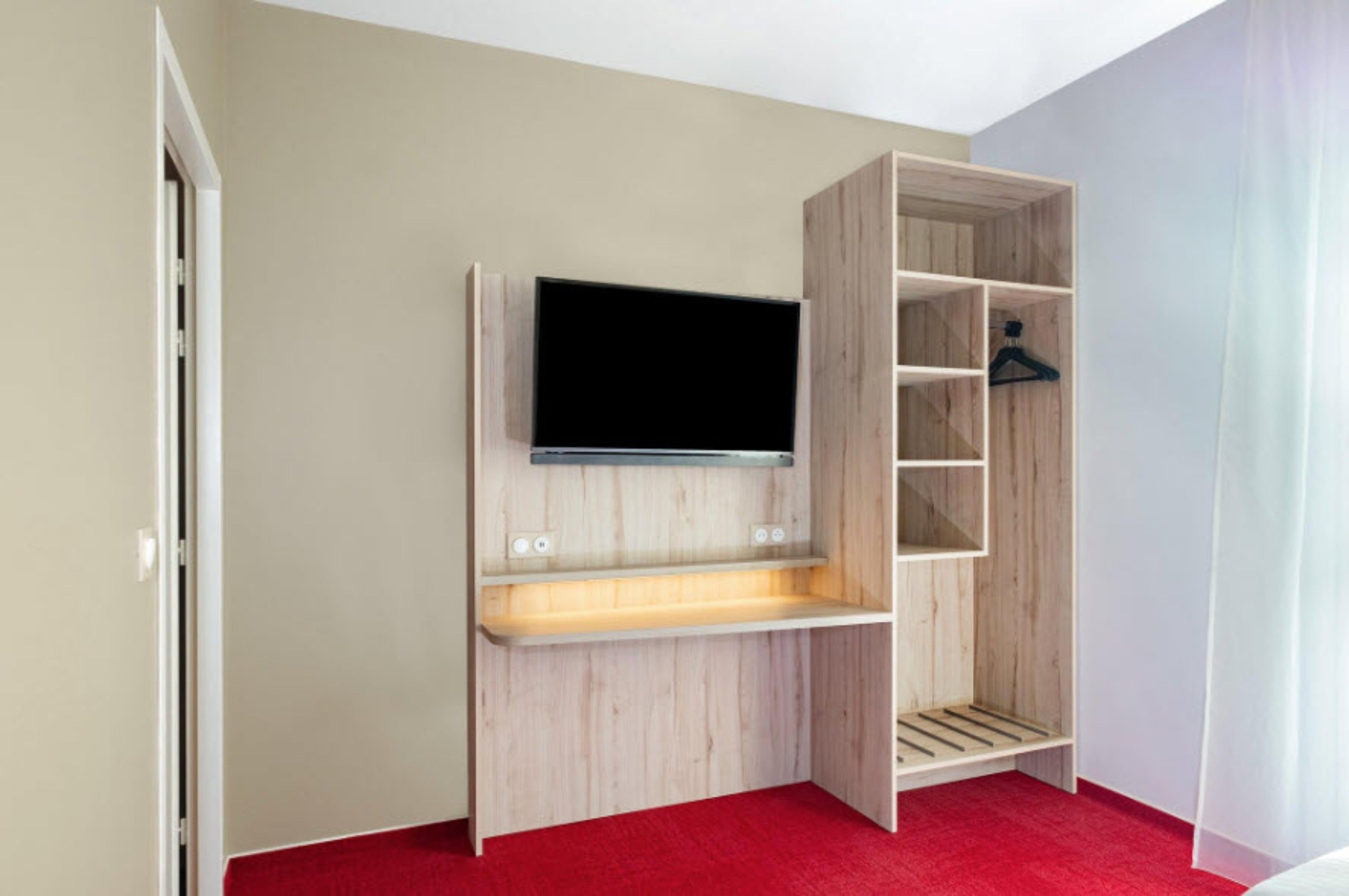 A room with a built-in TV shelf, a red carpet, and a wooden wardrobe with multiple compartments.
