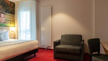 Une chambre d’hôtel avec un lit, un fauteuil vert, une table en bois et un radiateur.