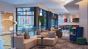 A modern hotel lobby with a sectional sofa, a glass railing, and a view of the cityscape. - Hyatt Place Indianapolis Downtown (Indianapolis)