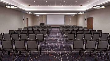 Une salle de conférence avec des rangées de chaises, un grand écran et un pupitre.