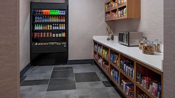 A small kitchenette area with a refrigerator stocked with beverages, a microwave, and a shelf with packaged snacks.