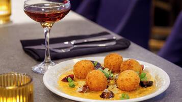 A plate of croquettes with a side of sauce, a glass of red wine, and a candle on a table.