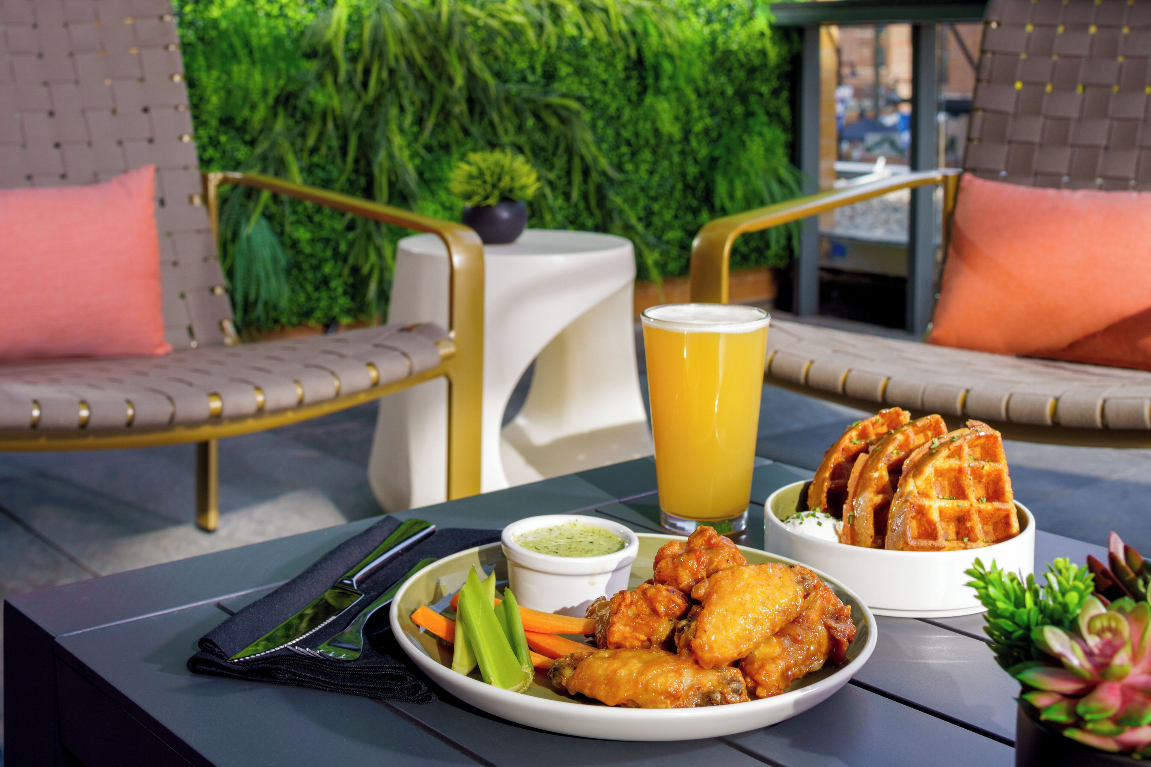 A table with a plate of chicken wings, a glass of orange juice, and a bowl of waffles.