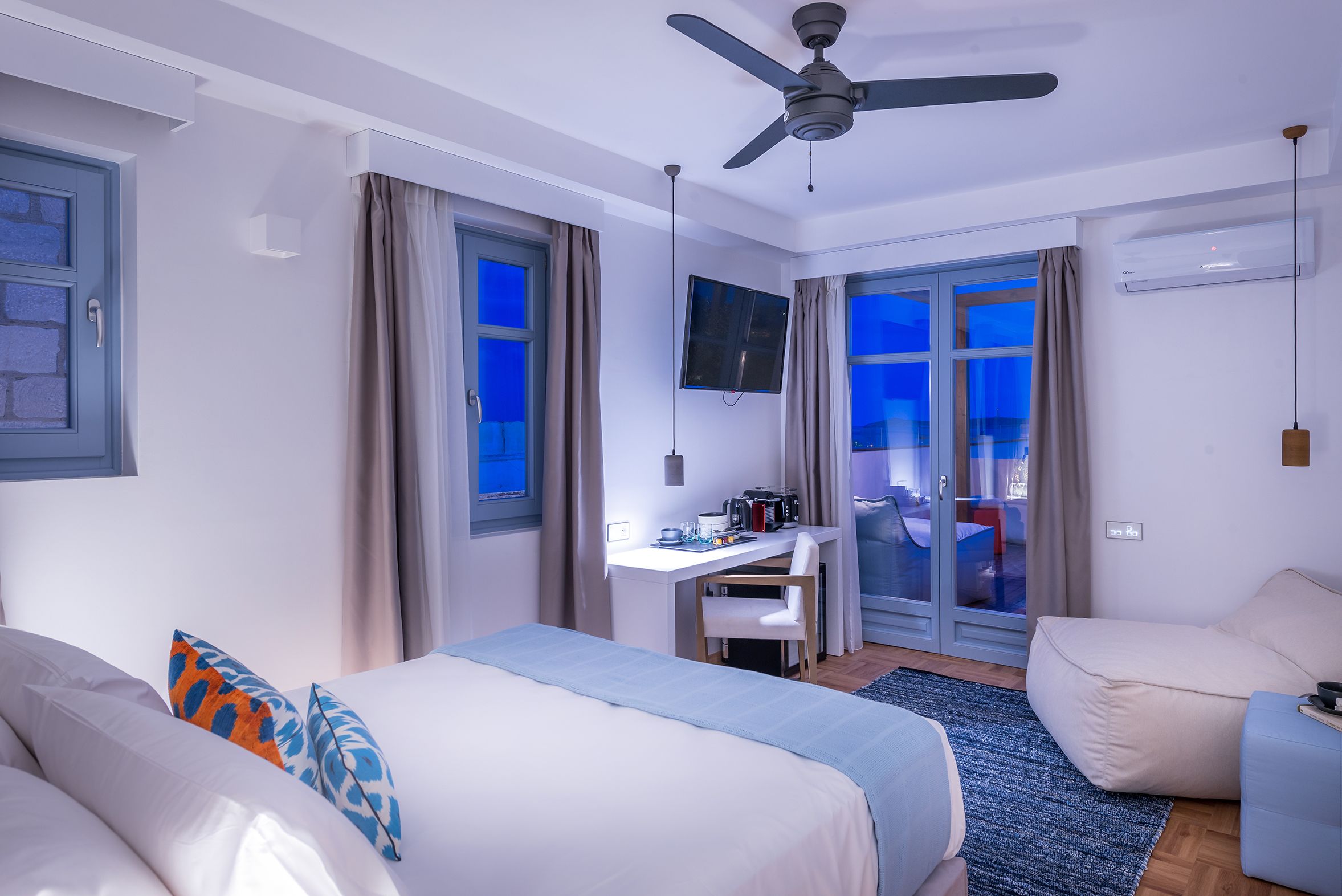 A hotel room with a bed, desk, chair, and a view of the city at night.