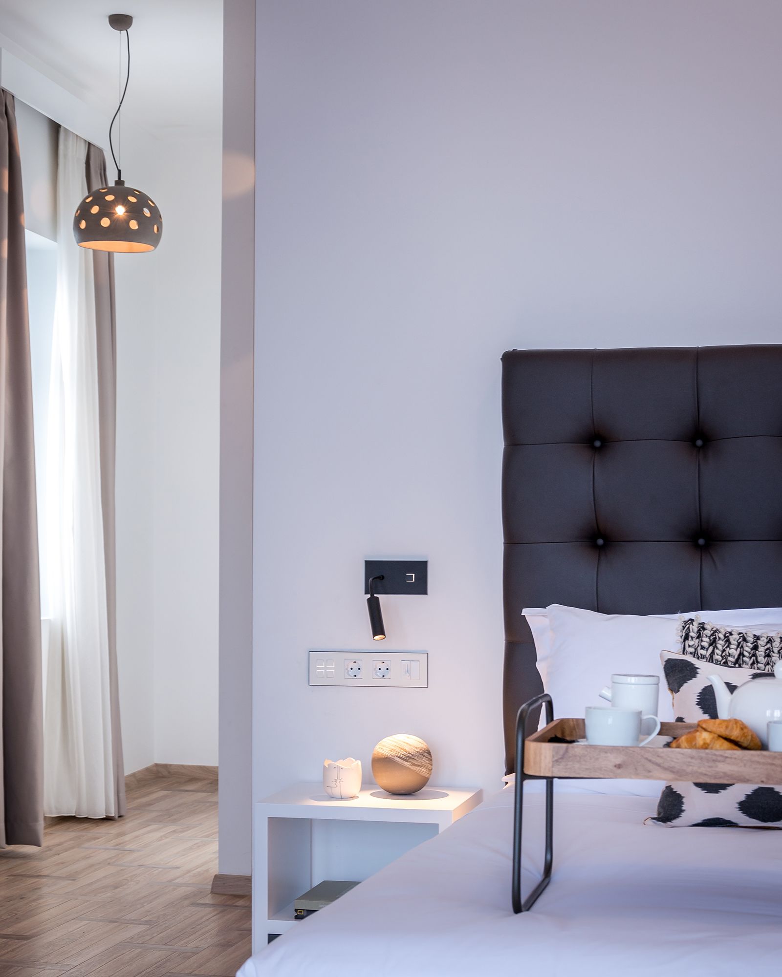 Ein modernes Schlafzimmer mit einem gepolsterten Kopfteil, einem Nachttisch mit Lampe und einem Tablett mit Frühstücksangeboten.