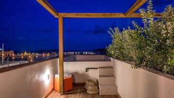 Uma varanda com pérgola de madeira, um espaço de estar pequeno e vista para a cidade à noite.