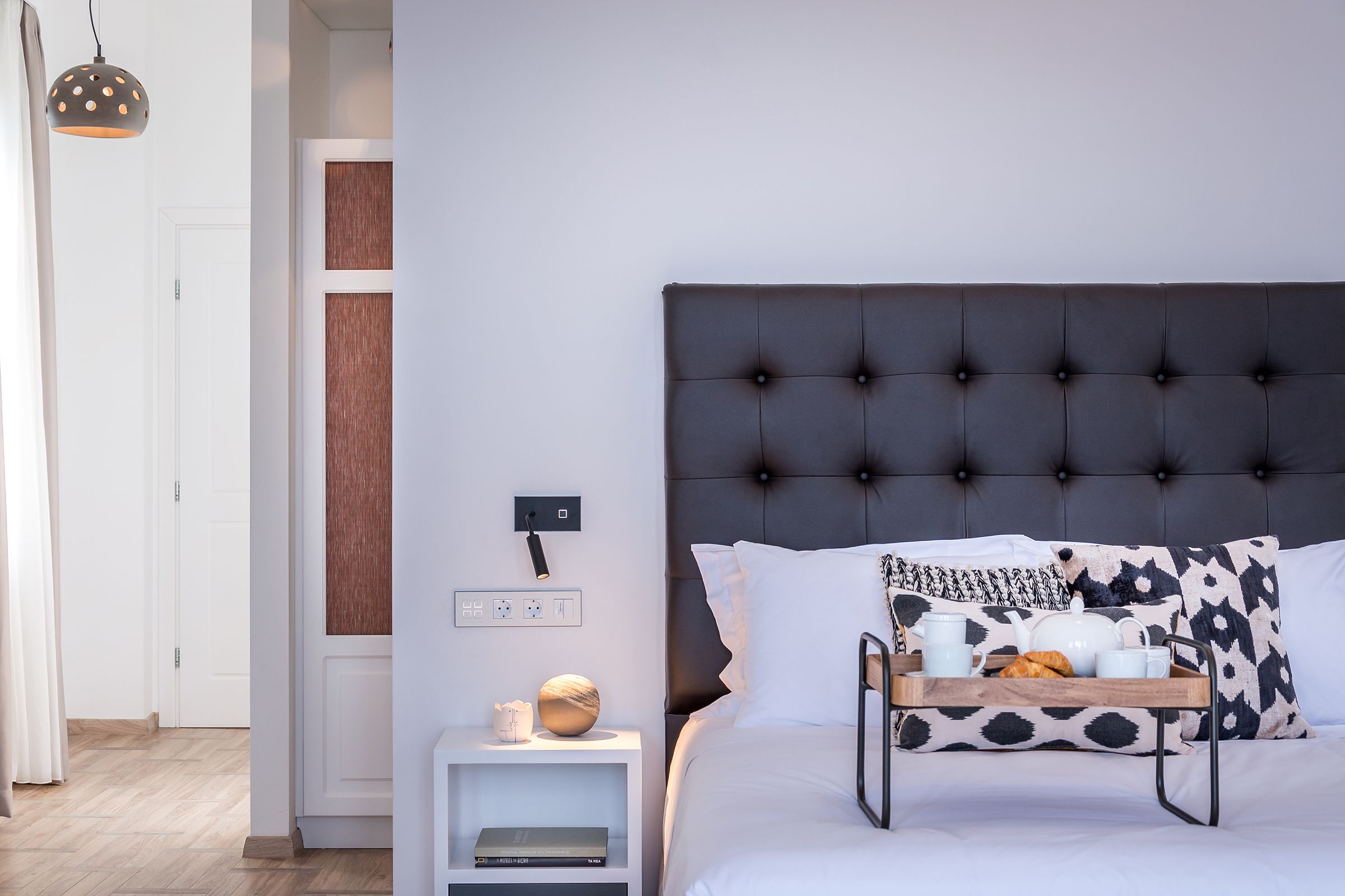 A modern bedroom with a tufted headboard, a bedside table with a lamp, and a tray with breakfast items.