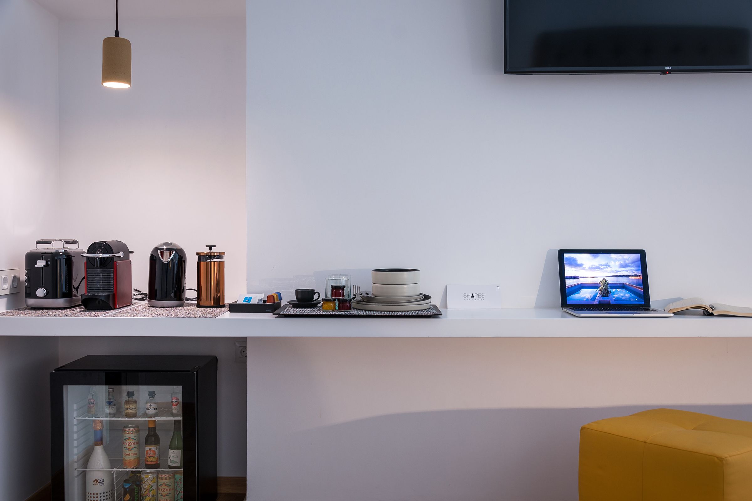 Uma cozinha moderna com geladeira, cafeteiras e um laptop no balcão.