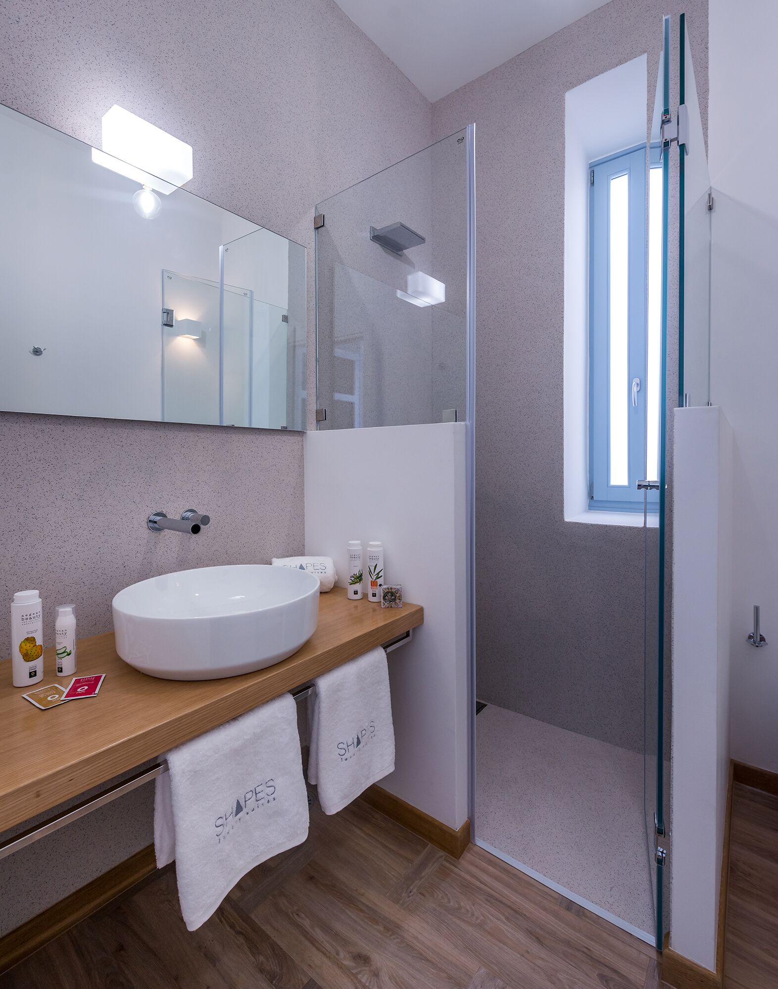 Un baño moderno con un lavamanos blanco grande, cabina de ducha de vidrio y ventana con vistas azules.