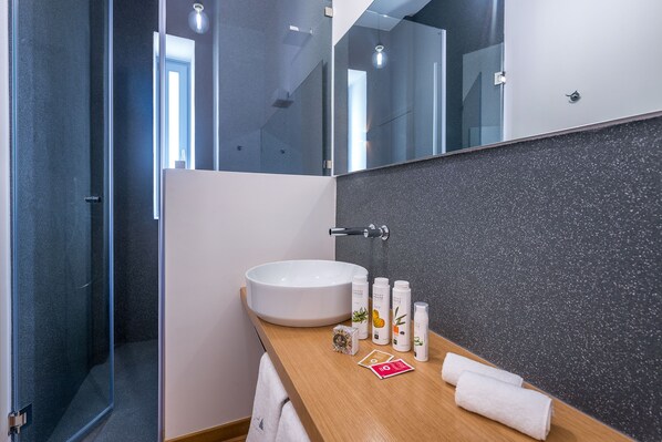A modern bathroom with a large white sink, a glass shower enclosure, and a wooden vanity with toiletries.