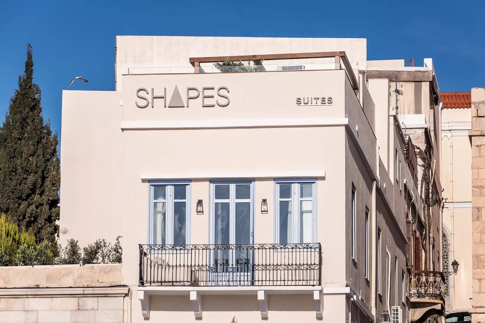 A building with a sign reading "SHAPES SUITES" and a balcony with a wrought iron railing.