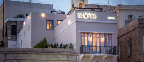 A hotel named 'SHAPES' with a prominent tower, a 'TRAVEL RENT A CAR' sign, and various shops on the ground floor.