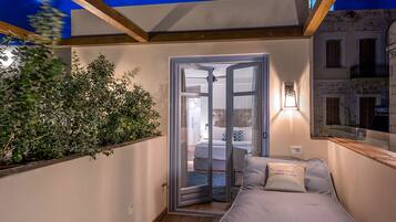 A cozy balcony with a wooden floor, a comfortable bed, and a view of the city at night.
