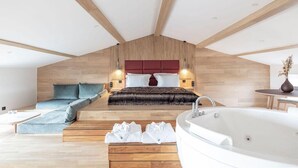 Ein modernes Schlafzimmer mit schrägem Dach, einem großen Bett mit rotem Kopfteil, einer Sitzecke mit Sofa, einer Badewanne und Holzboden.