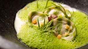 Ein Gericht mit Ravioli, garniert mit Kräutern und Croutons, serviert mit grüner Soße.
