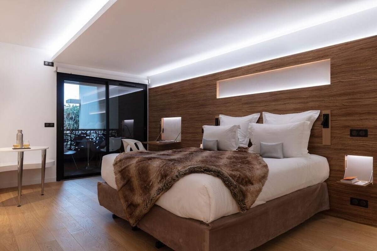 Un dormitorio moderno con una cama grande, paneles de madera en la pared y un ventanal de vidrio que da a un espacio exterior.