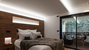 Ein modernes Schlafzimmer mit Holz-Kopfteil, einem großen Bett mit weißer Bettwäsche, einem Nachttisch mit Lampe und einem Balkon mit Gartenmöbeln.