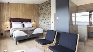 Quarto moderno com uma cama grande, duas mesas de cabeceira, uma parede com detalhes em pedra e vista para o exterior.