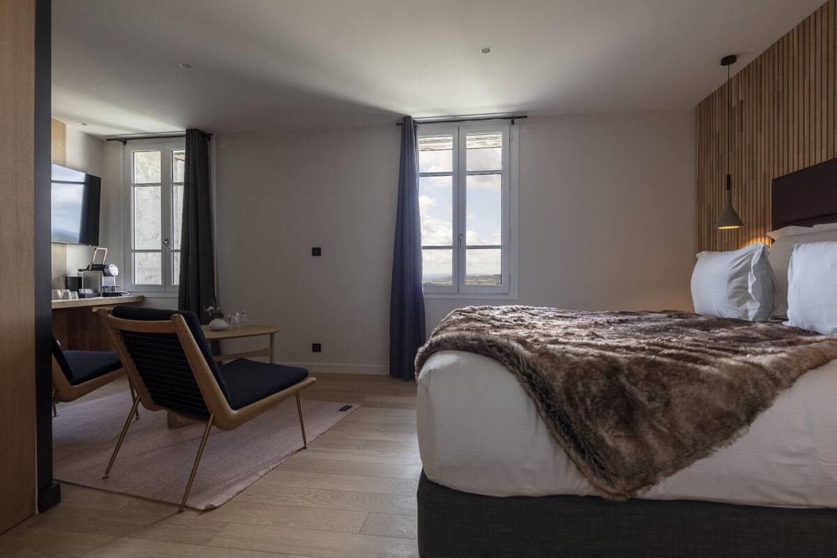 Un dormitorio moderno con una cama grande, un escritorio con una silla y vistas al exterior a través de las ventanas.