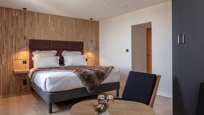 Quarto moderno com cama grande, abajures, mesa redonda com um vaso e painéis de parede de madeira.