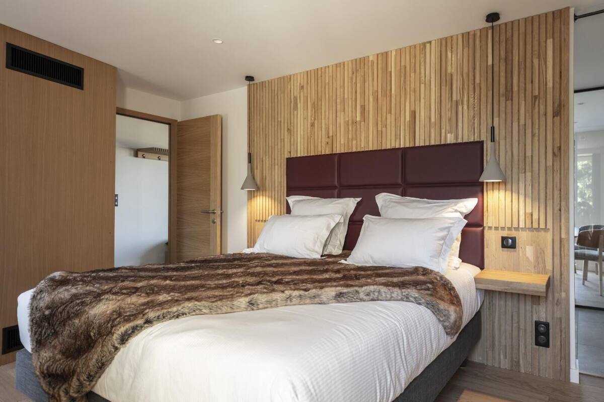 Un dormitorio moderno con cabecera de madera, una cama grande con ropa de cama blanca y un cubrecama de piel.
