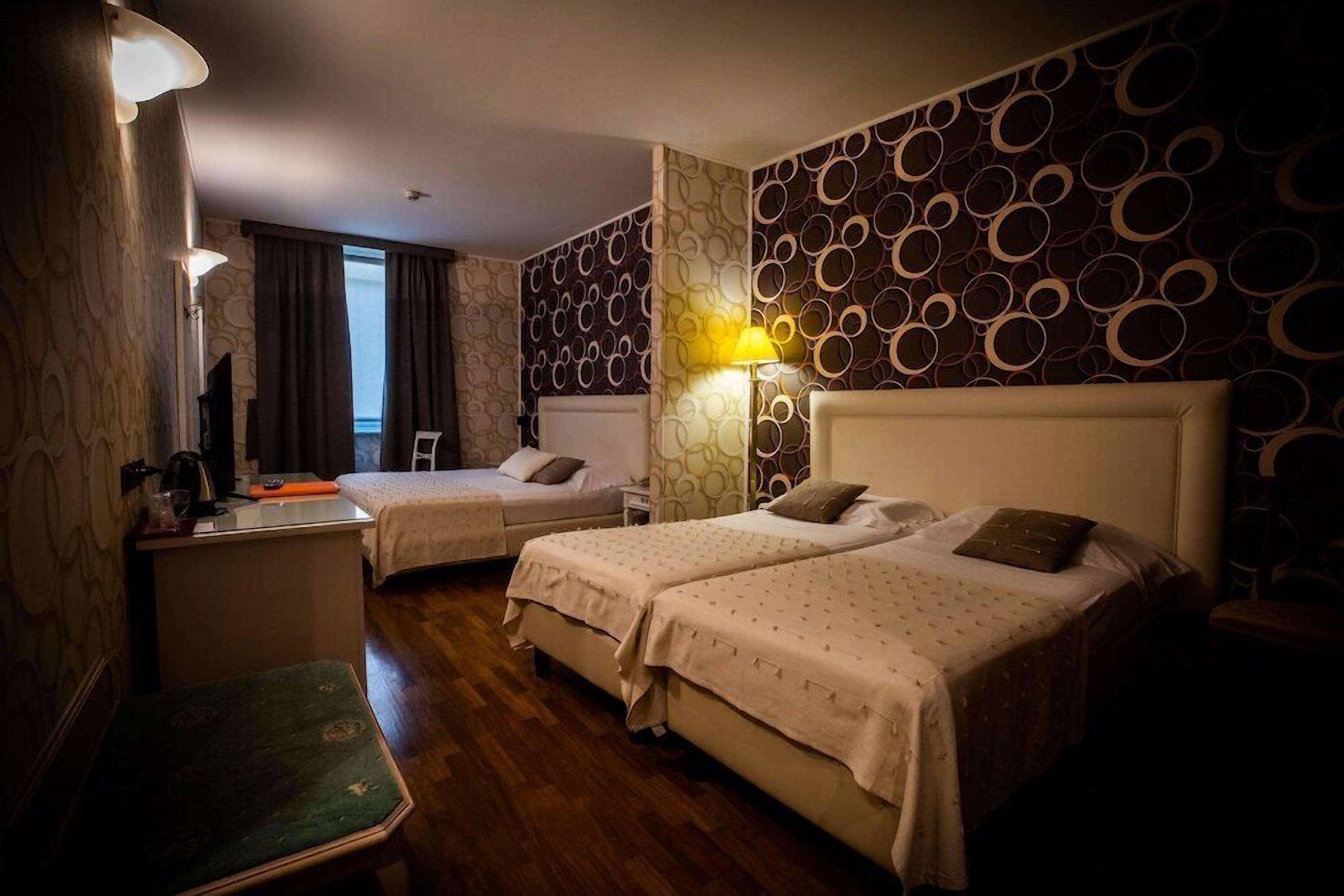 A hotel room with two beds, a desk, a chair, and a view of the sea.