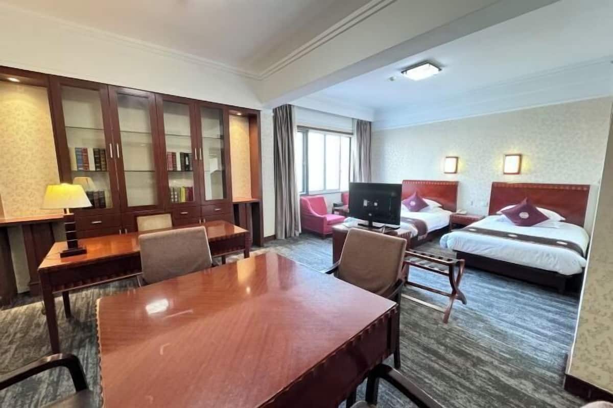 Ein Hotelzimmer mit Schreibtisch aus Holz, zwei Betten, einem Fernseher und einer Sitzecke.