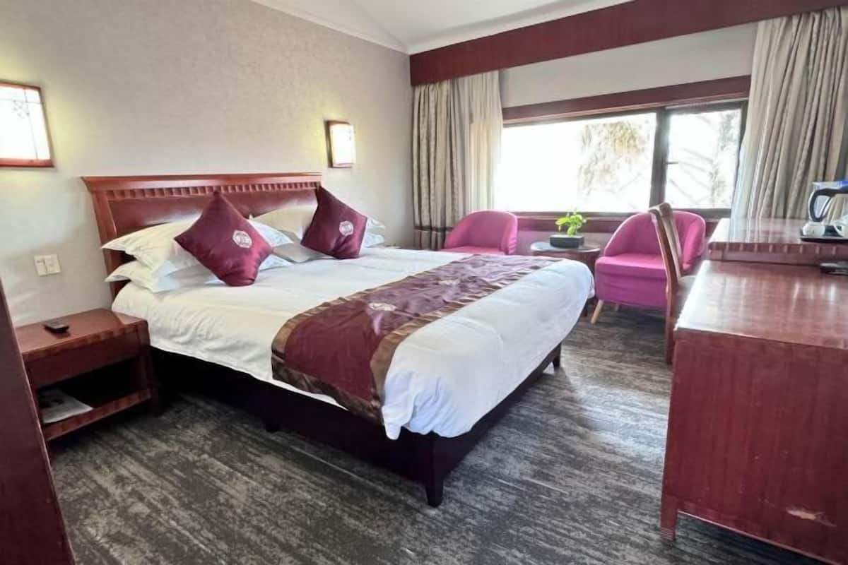 Ein Hotelzimmer mit einem großen Bett, zwei Nachttischen, einem Schreibtisch und einem Sessel.