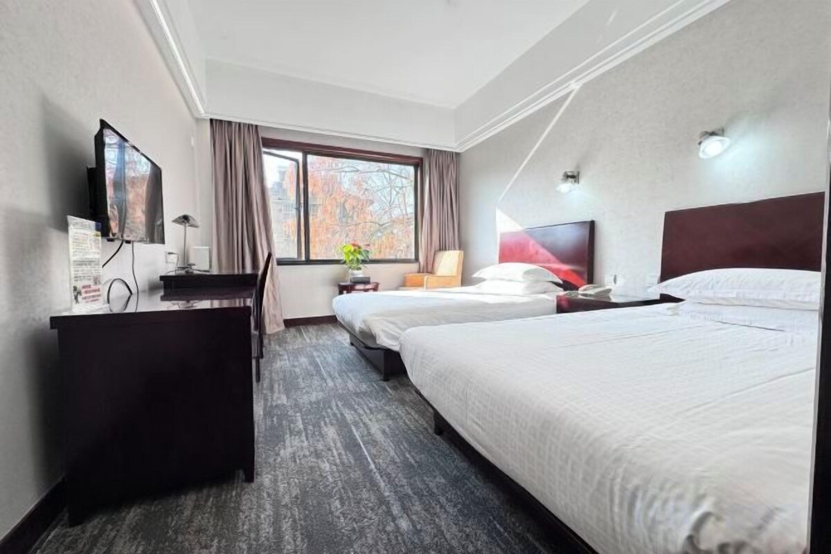 A hotel room with a bed, a desk, a chair, a television, and a window with curtains.