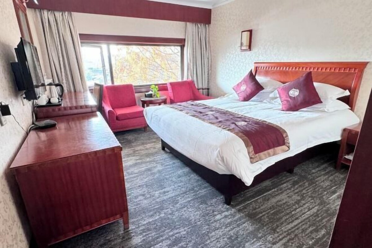 A hotel room with a large bed, a desk, a chair, and a window with curtains.