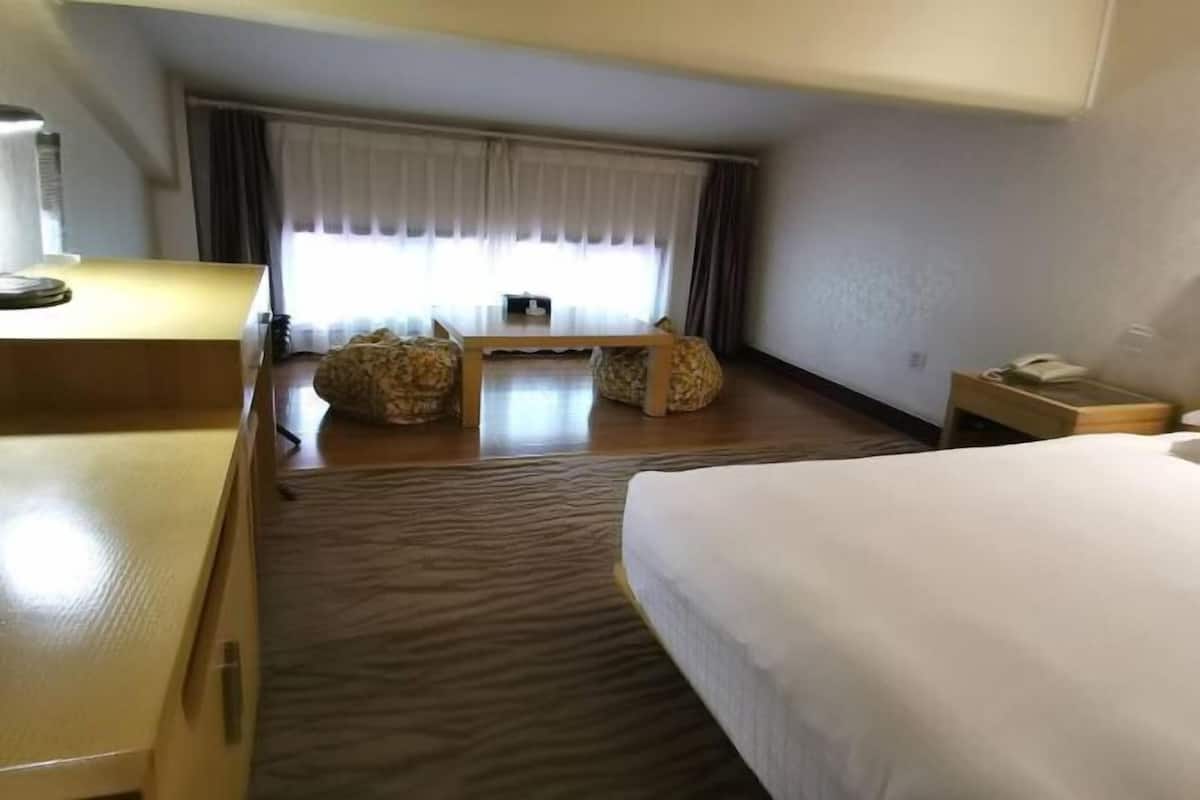 Ein Hotelzimmer mit Bett, Schreibtisch, Stuhl, kleinem Tisch und einem Fenster mit Vorhängen.