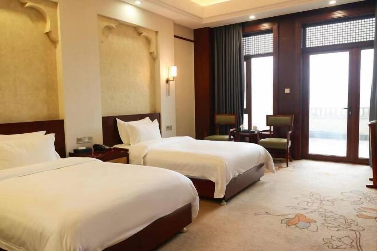 A hotel room with two beds, a desk, a chair, and a large window.
