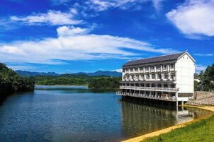 Un edificio de varios pisos con techo plano, situado sobre pilotes sobre una masa de agua, con cielo despejado y montañas al fondo.