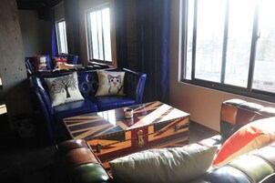 Una sala de estar con un sofá azul, una mesa de centro estampada y una ventana con cortinas.