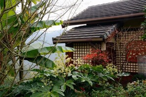 A traditional Japanese building with a tiled roof, surrounded by lush greenery and flowering plants.