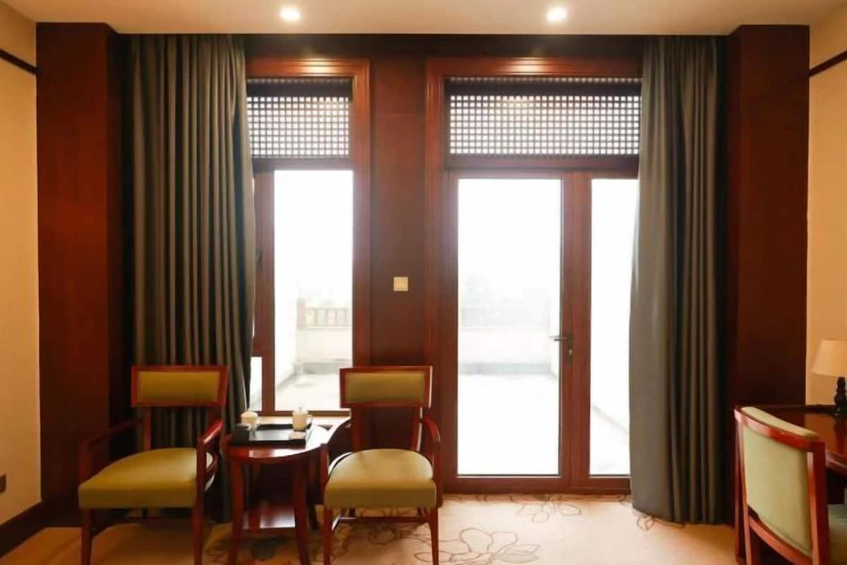 A hotel room with a balcony, a dining table with chairs, and a small desk with a lamp.