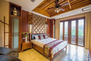 A spacious bedroom with a large bed, wooden ceiling, and a balcony with a view.