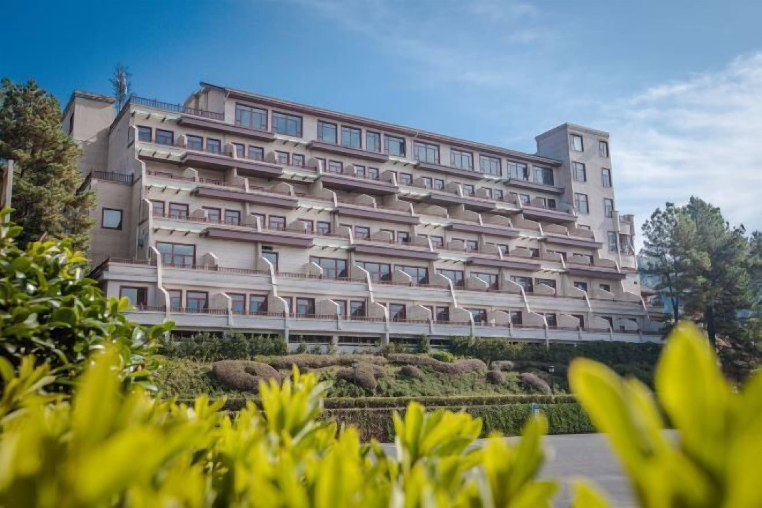 A multi-story hotel with a modern architectural design, featuring balconies and a landscaped garden area in the foreground.