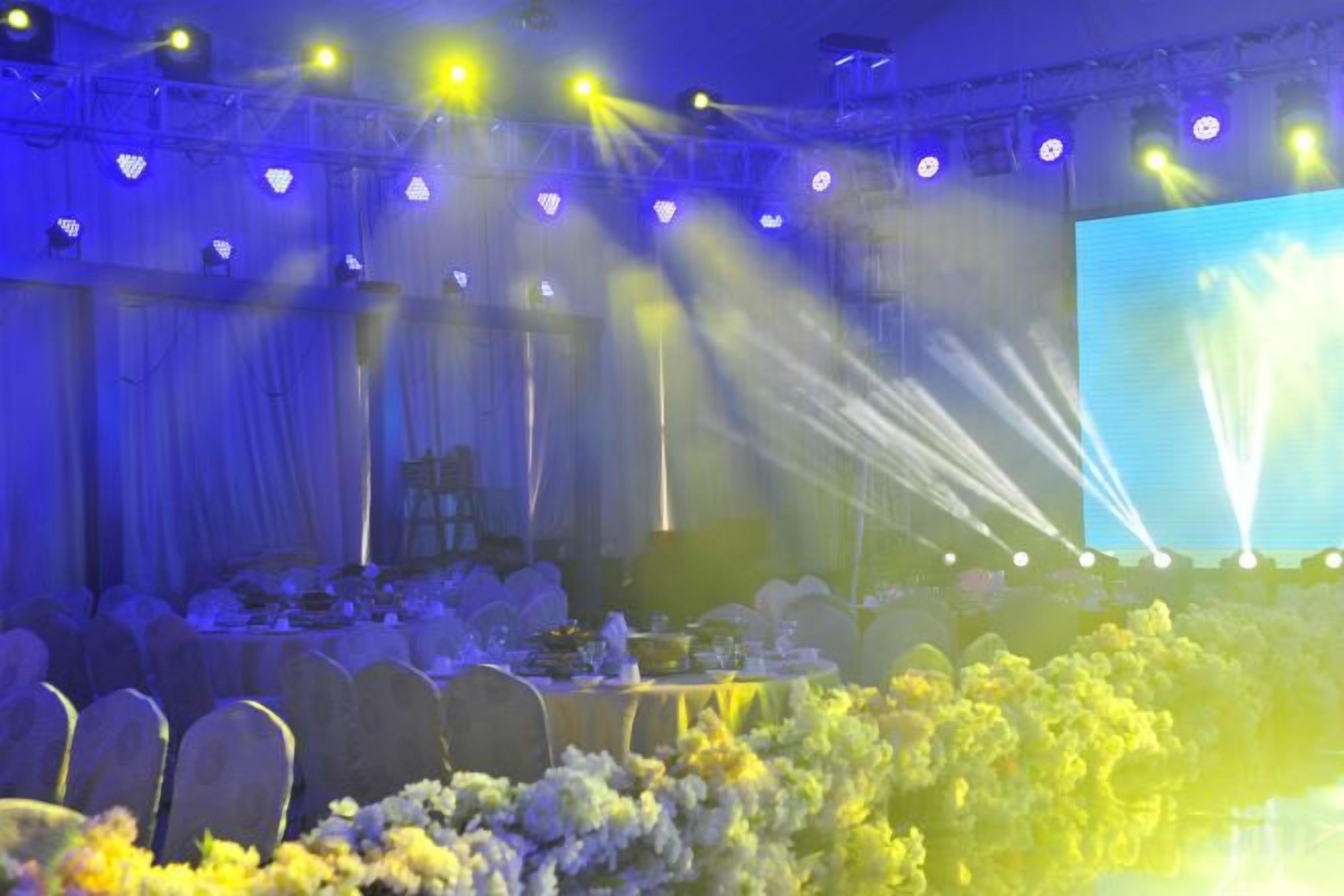 A banquet hall with tables set for an event, a stage with a large screen, and stage lighting.