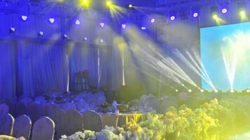 A banquet hall with tables set for an event, a stage with a large screen, and stage lighting.