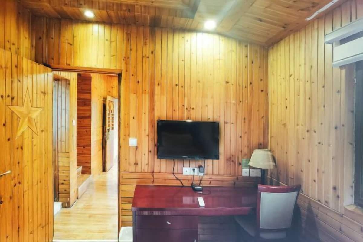 A wooden-paneled room with a desk, chair, and a television mounted on the wall.