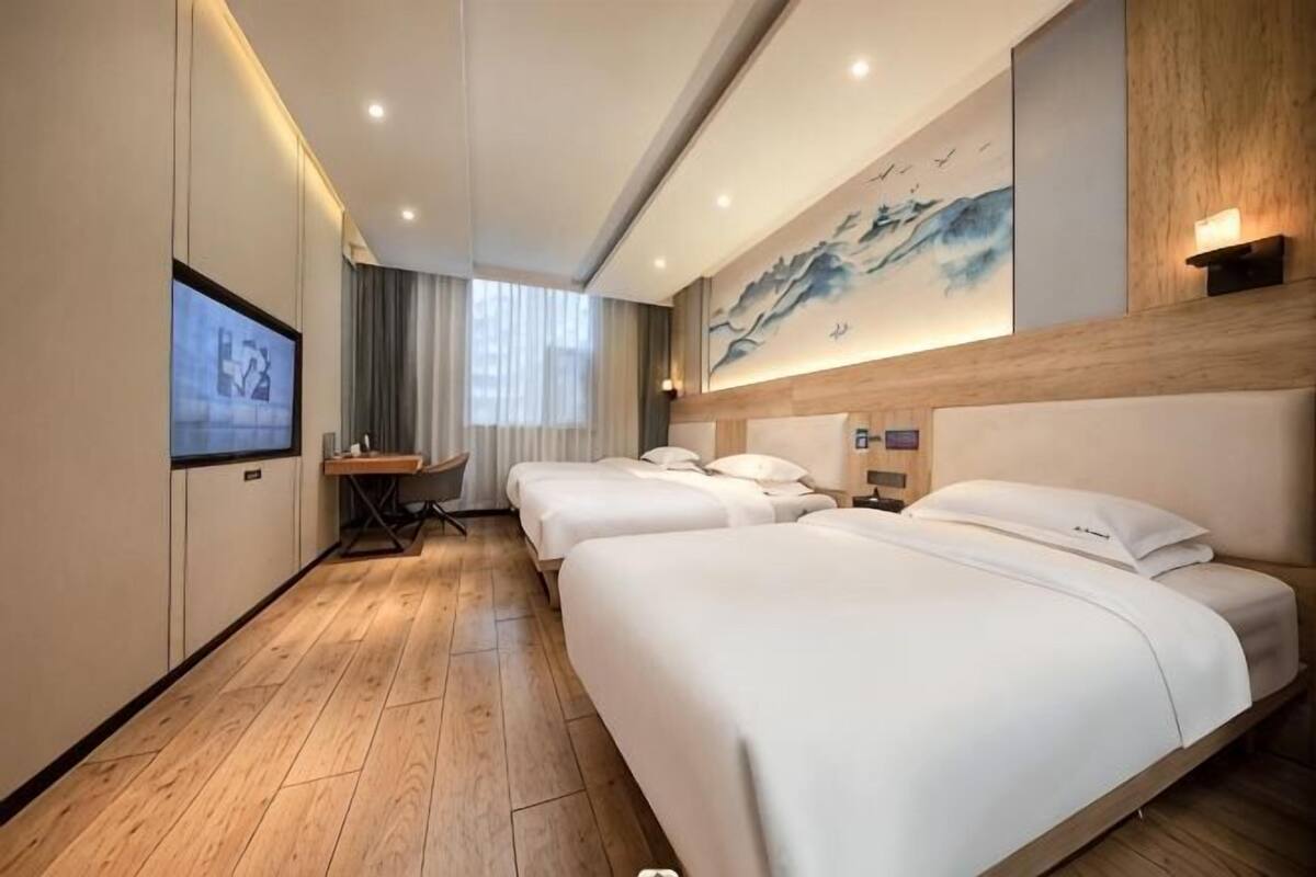 A hotel room with three beds, a TV, a desk, and a painting on the wall.