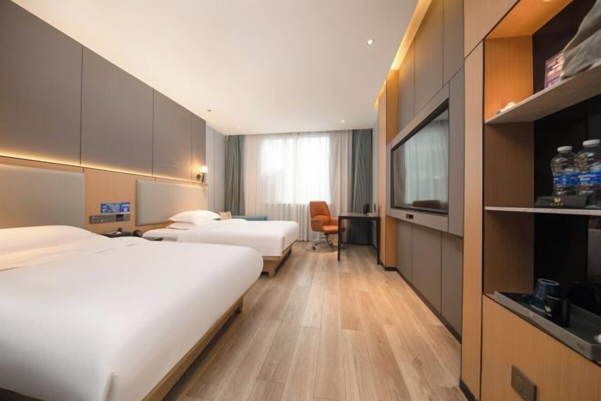 A hotel room with two beds, a desk, a chair, a TV, and a minibar.