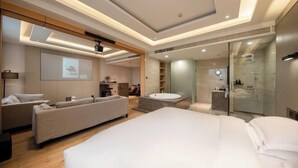 Une chambre d’hôtel moderne dotée d’un grand lit, d’un canapé, d’un petit bureau, d’une baignoire et d’une cabine de douche en verre.