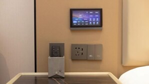 Une chambre d’hôtel équipée d’un panneau de commande au mur, d’une prise de courant et d’un haut-parleur sur la table.