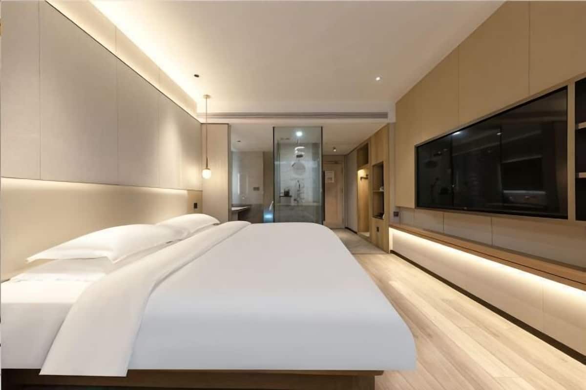 A modern hotel room with a large bed, a walk-in closet, and a large window.