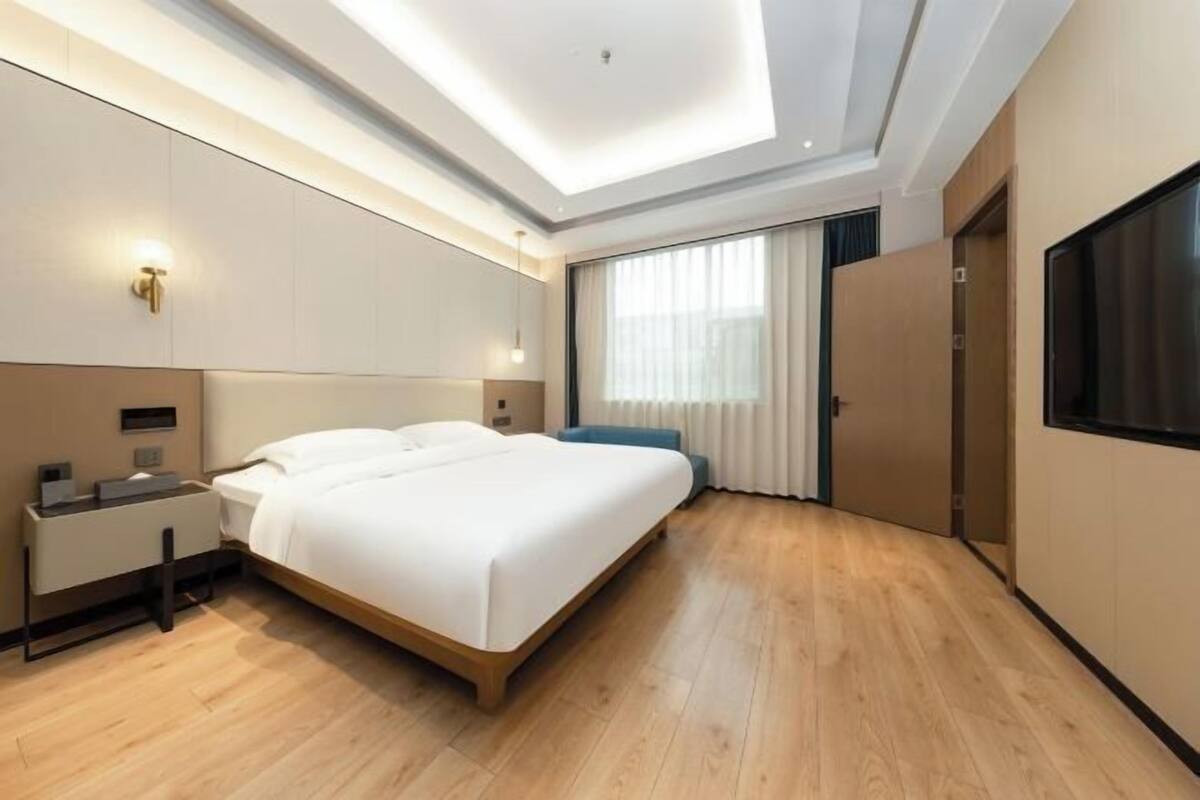 A modern hotel room with a large bed, bedside tables, a desk, and a large window with curtains.