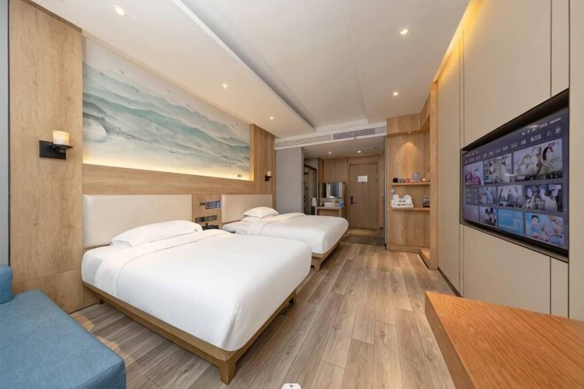 A hotel room with two beds, a desk, a TV, and a wooden floor.